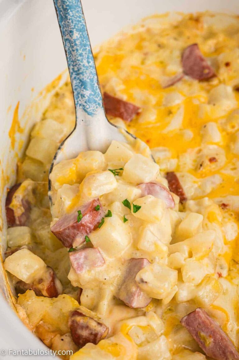 cheesy chopped potatoes and sliced kielbasa cooked in a slow cooker. top down view with spoon ladling out ingredients.