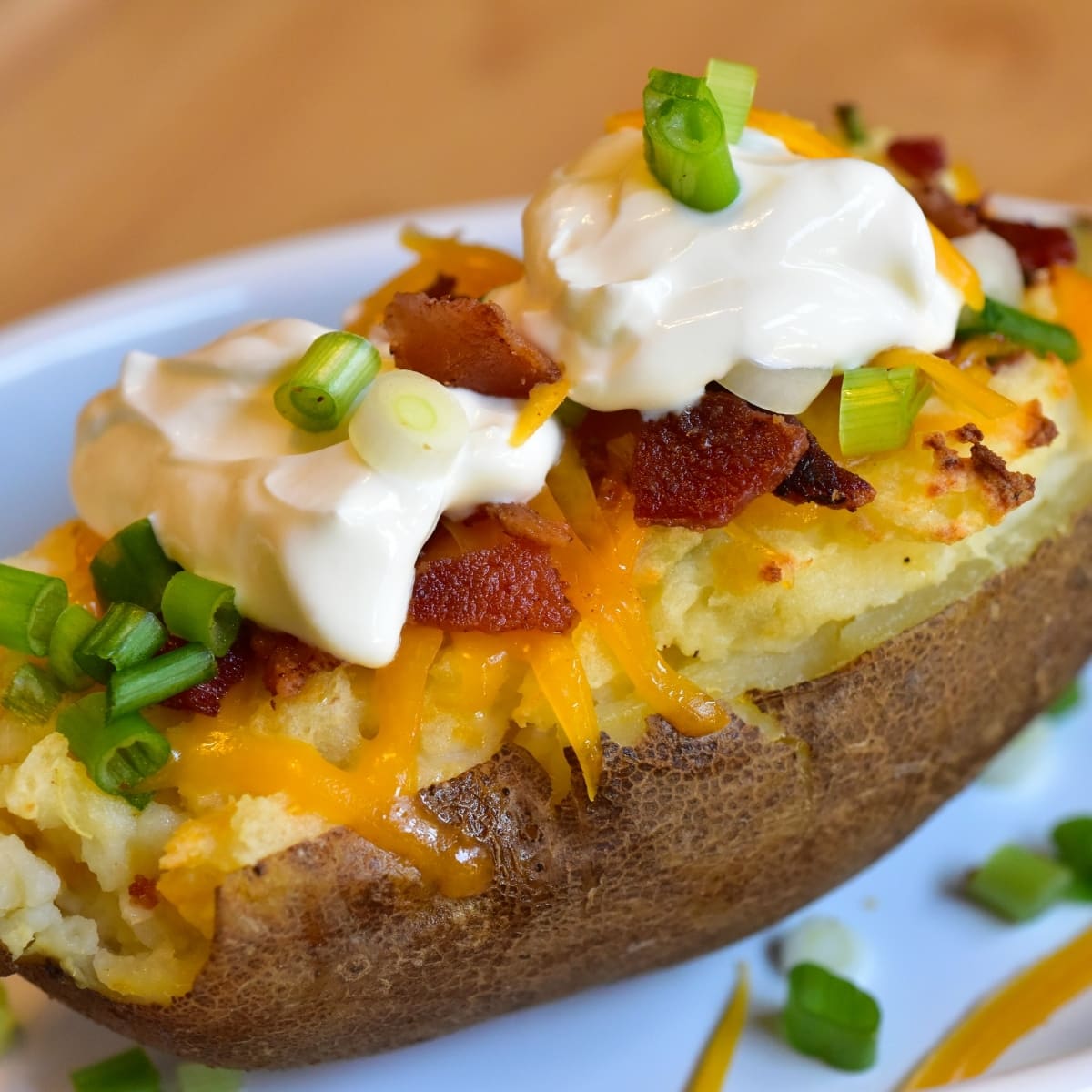 Air fryer baked potato close up topped with shredded cheese, chopped bacon, sour cream and sliced green onions.