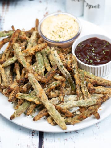 air fryer breaded green beans arranged on a plate with 2 types of dips