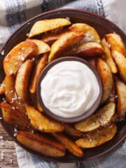 air fryer potato wedges on a plate with dip in the middle. Top down view.