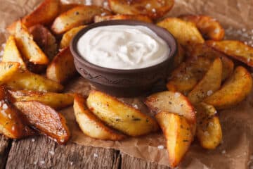 air fryer potato wedges on brown paper with ranch dressing in a bowl for dipping
