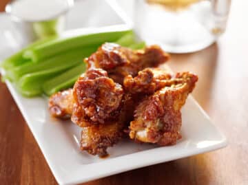 oven baked buffalo chicken wings served on a white platter with celery, dip and beer
