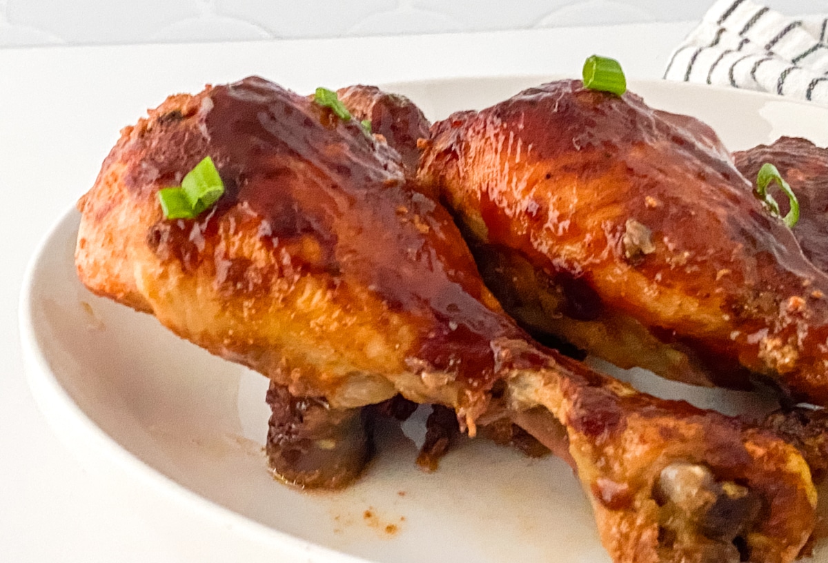 Close up and side view of Slow cooker bbq chicken legs on a white plate.