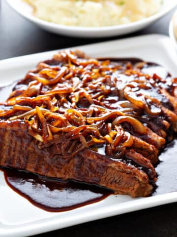 beef brisket served on a white plate with caramelized onions on arranged over the top