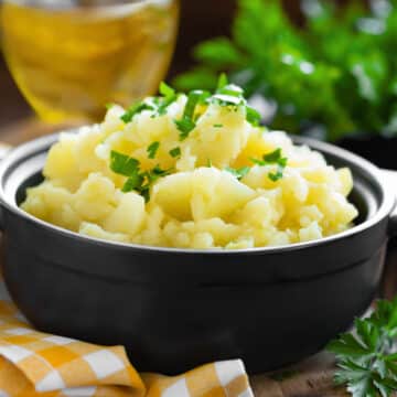 cream cheese mashed potatoes in a dark ceramic bowl garnished with parsley
