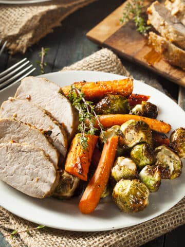 Instant Pot Pork Roast carved and served with roasted carrrots and brussels sprouts.