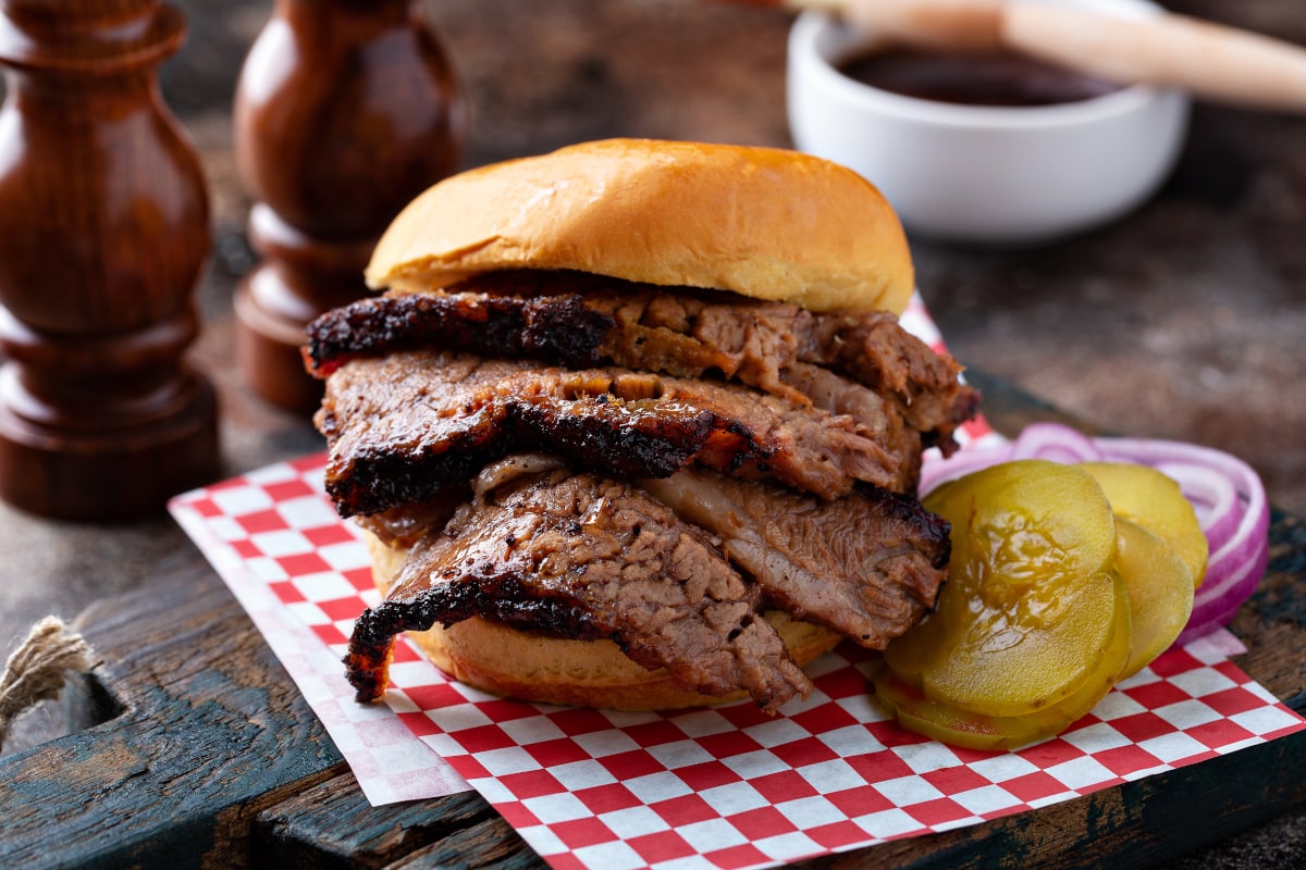 sliced beef brisket served on a bun with au jus and pickles on the side.