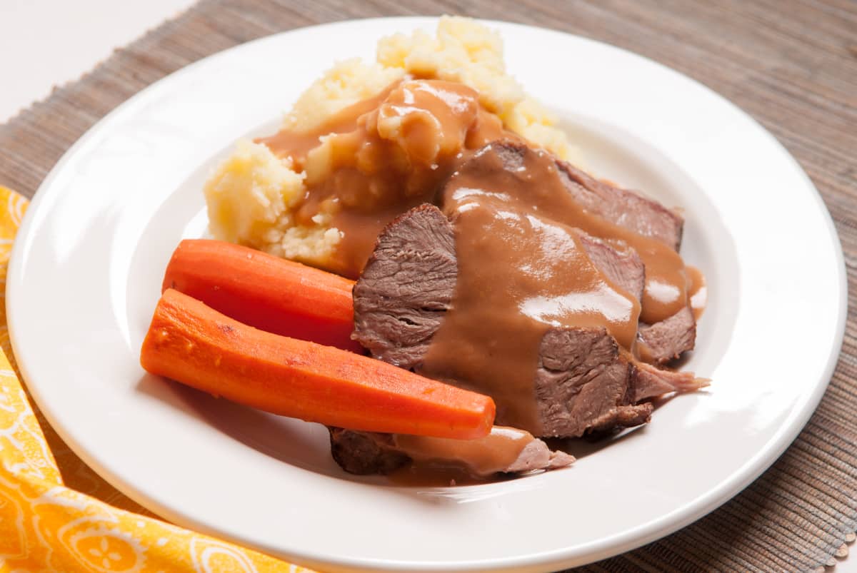 Oven baked chuck roast recipe served with potatoes and carrots and drizzled with gravy