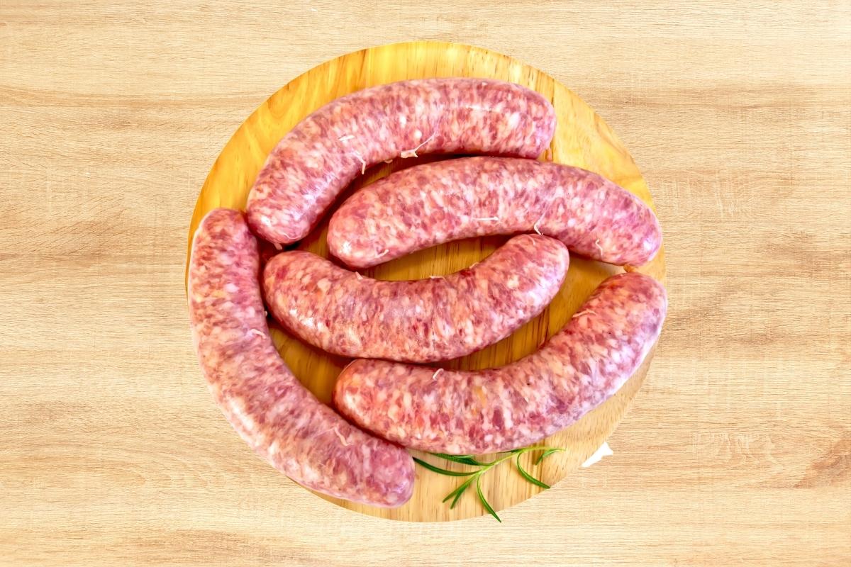 5 fresh italian sausages on a wooden board top down