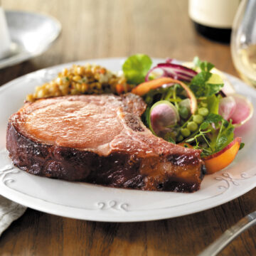 thick cut pork chop served on a white plate with a side salad