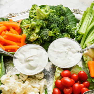 a veggies tray with 2 dips and an assortment of broccoli, carrots, celery, cherry tomatoes and cauliflower closeup