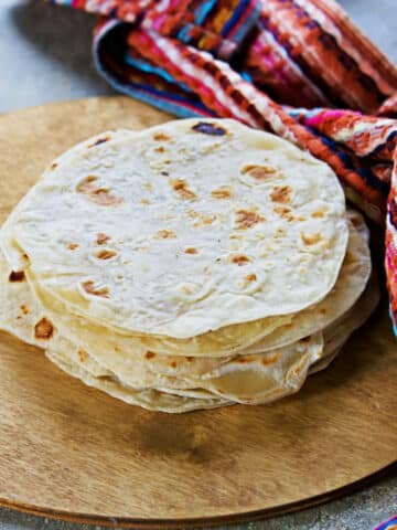 how to warm flour tortillas - set on a wooden plate with a colorful tea towel