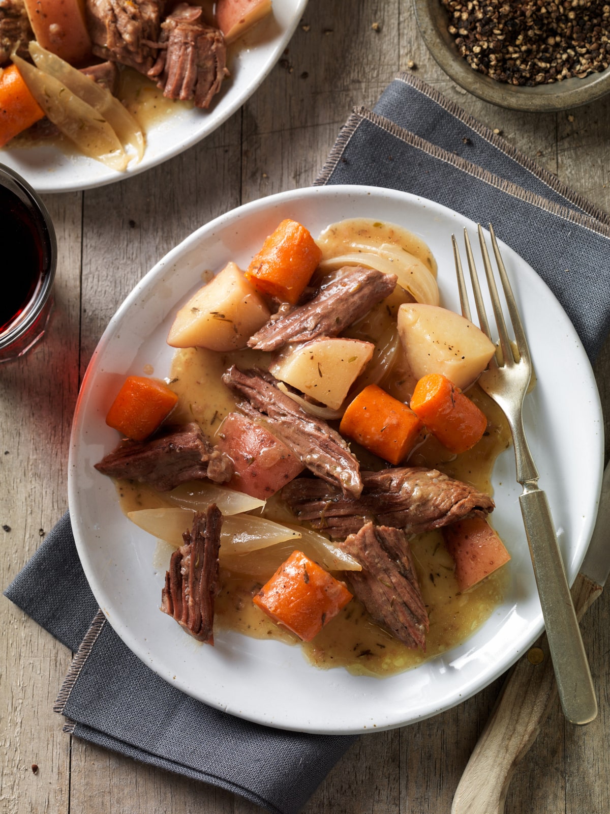 Beef pot roast pieces on a plate with roasted carrots, potatoes, and onions served with gravy.
